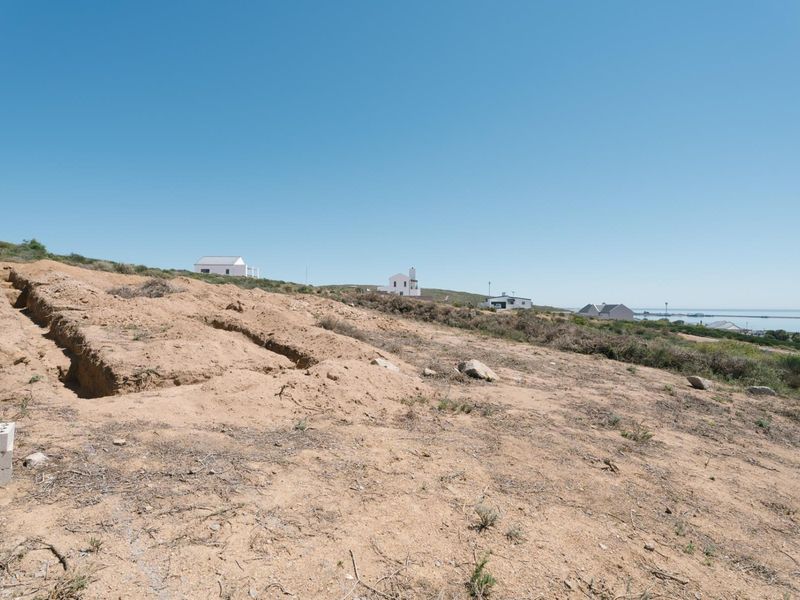 A vacant residential plot featuring sloped terrain and an existing excavation trench, offering potential for development with distant coastal views.