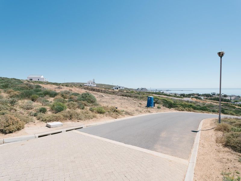 A view of the paved street and infrastructure bordering the vacant residential land, featuring coastal landscape views in the distance.