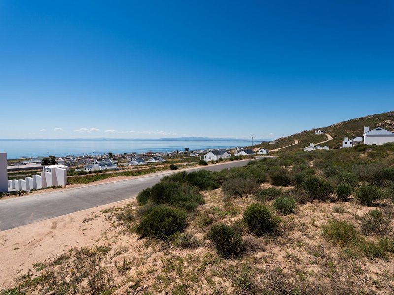 A scenic elevated view overlooking a coastal residential area with a paved road and natural vegetation in the foreground.