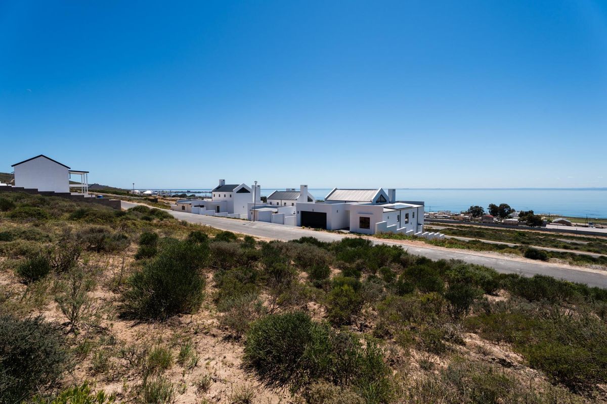 An elevated view of a coastal residential area featuring modern white homes situated along a paved road with ocean views.