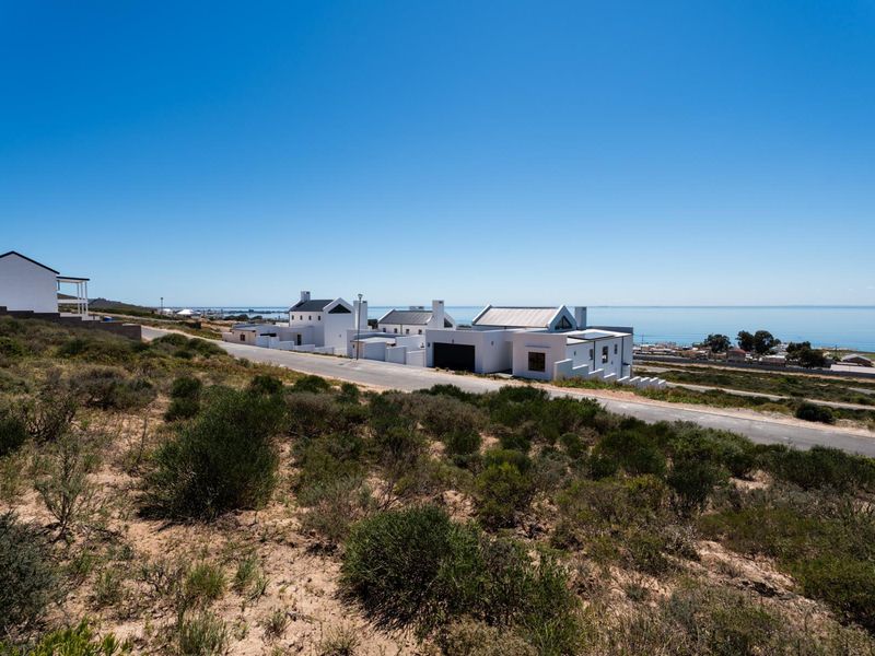 An elevated view of a coastal residential area featuring modern white homes situated along a paved road with ocean views.
