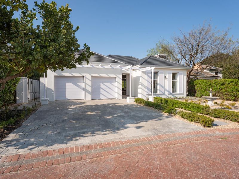 A well-maintained single-story residence featuring a double garage, paved driveway, and an elegant pergola entrance with manicured garden landscaping.