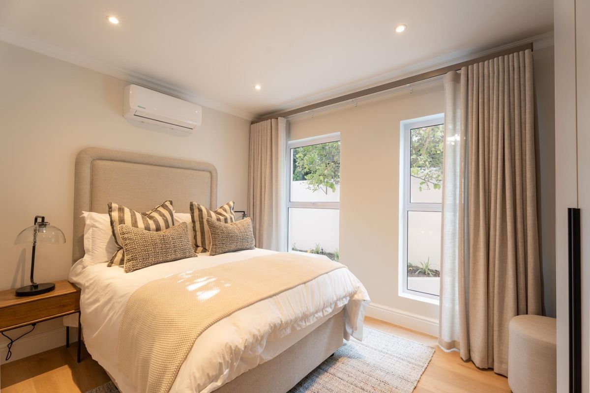 A well-maintained bedroom featuring timber flooring, recessed downlighting, and a wall-mounted air conditioning unit, complemented by natural light from dual windows.