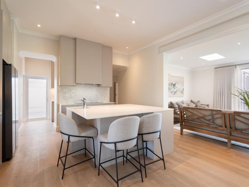 Modern open-plan kitchen and living area featuring a central island with stone countertops, integrated cabinetry, recessed lighting, and light hardwood flooring.