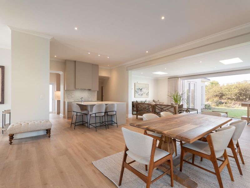 Spacious open-plan living area featuring a modern kitchen with island, light hardwood flooring, recessed lighting, and large sliding doors opening to the garden.