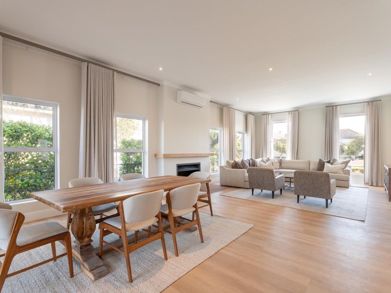Spacious open-plan living and dining area featuring light timber flooring, a built-in fireplace with a timber mantel, and abundant natural light through large windows.