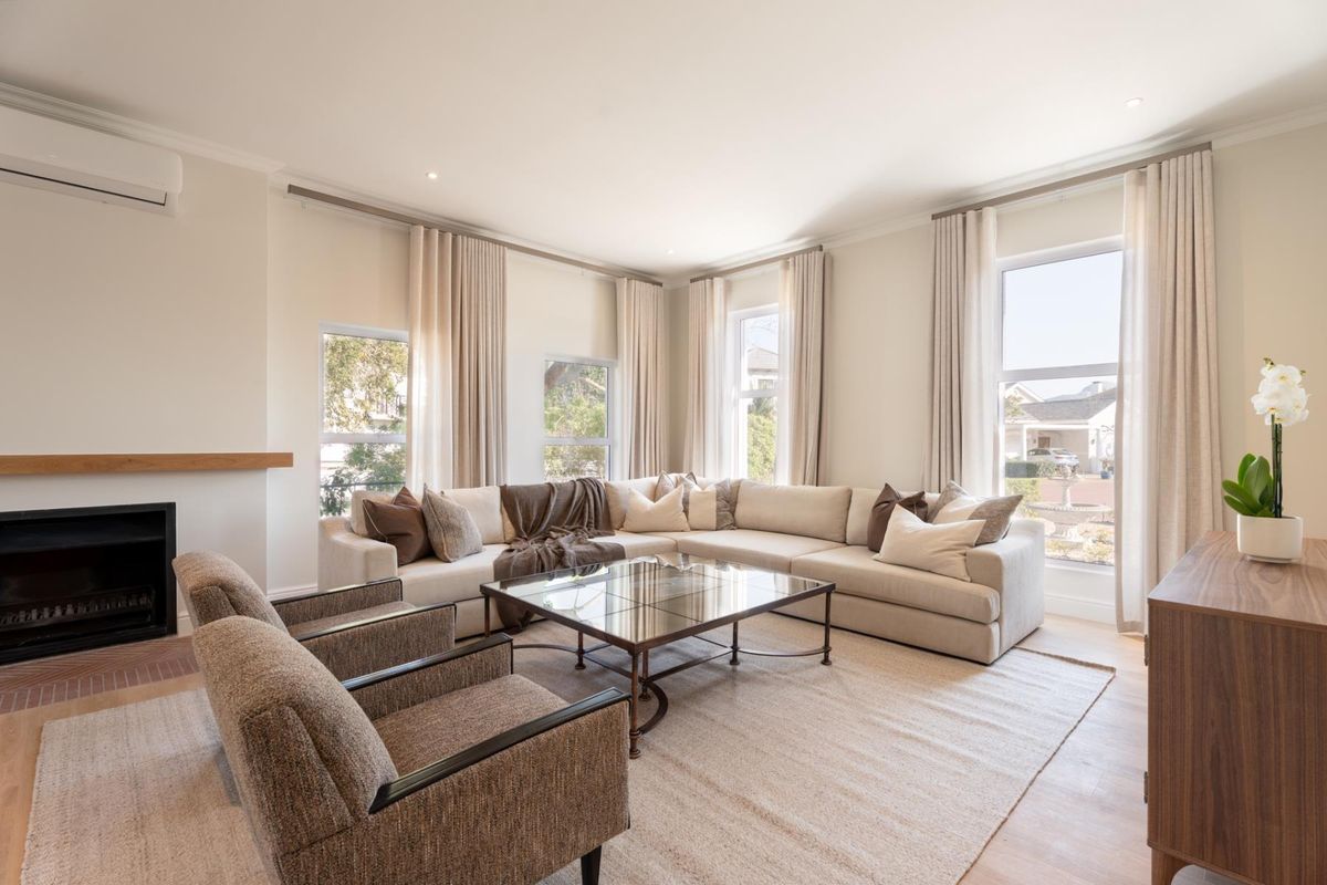 A bright and spacious living room featuring timber flooring, a built-in fireplace, and large windows with elegant drapery, creating a comfortable and inviting atmosphere.