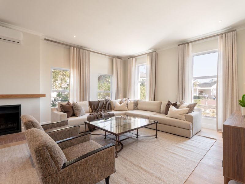A bright and spacious living room featuring timber flooring, a built-in fireplace, and large windows with elegant drapery, creating a comfortable and inviting atmosphere.
