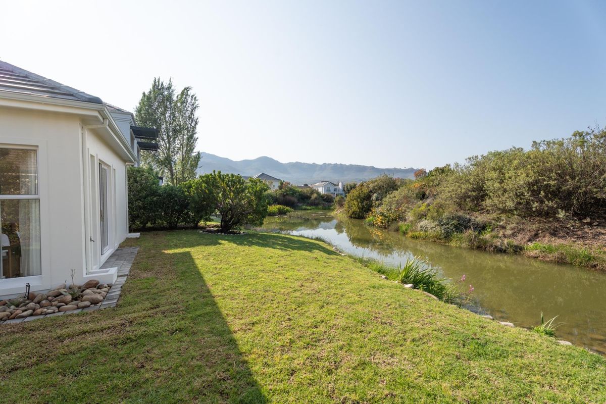 A well-maintained rear garden featuring a tranquil water feature, lush lawn, and scenic mountain views, directly accessible from the home's sliding glass doors.