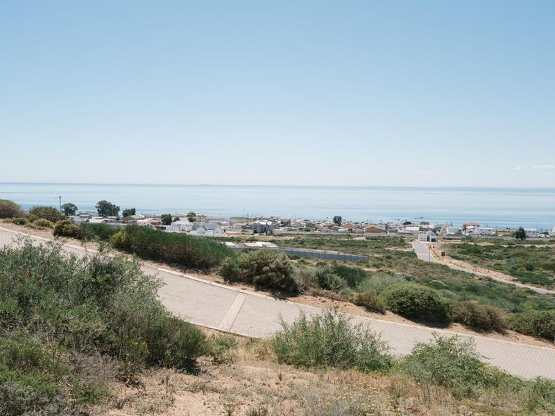 A scenic elevated view overlooking the coastal landscape and nearby residential area, featuring a paved access road in the foreground.