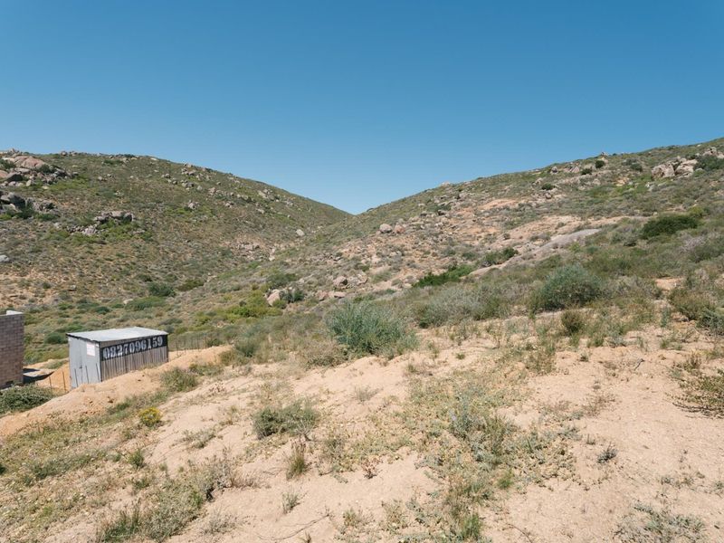 A view of a vacant residential plot featuring natural rocky terrain and a small metal storage shed.
