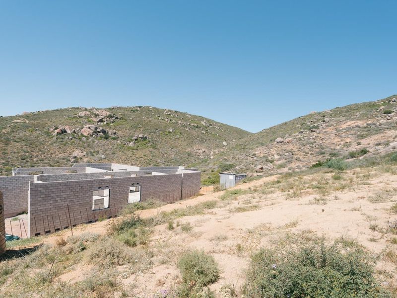 A view of a residential property under construction with concrete block walls and a water storage tank set against a hilly landscape.