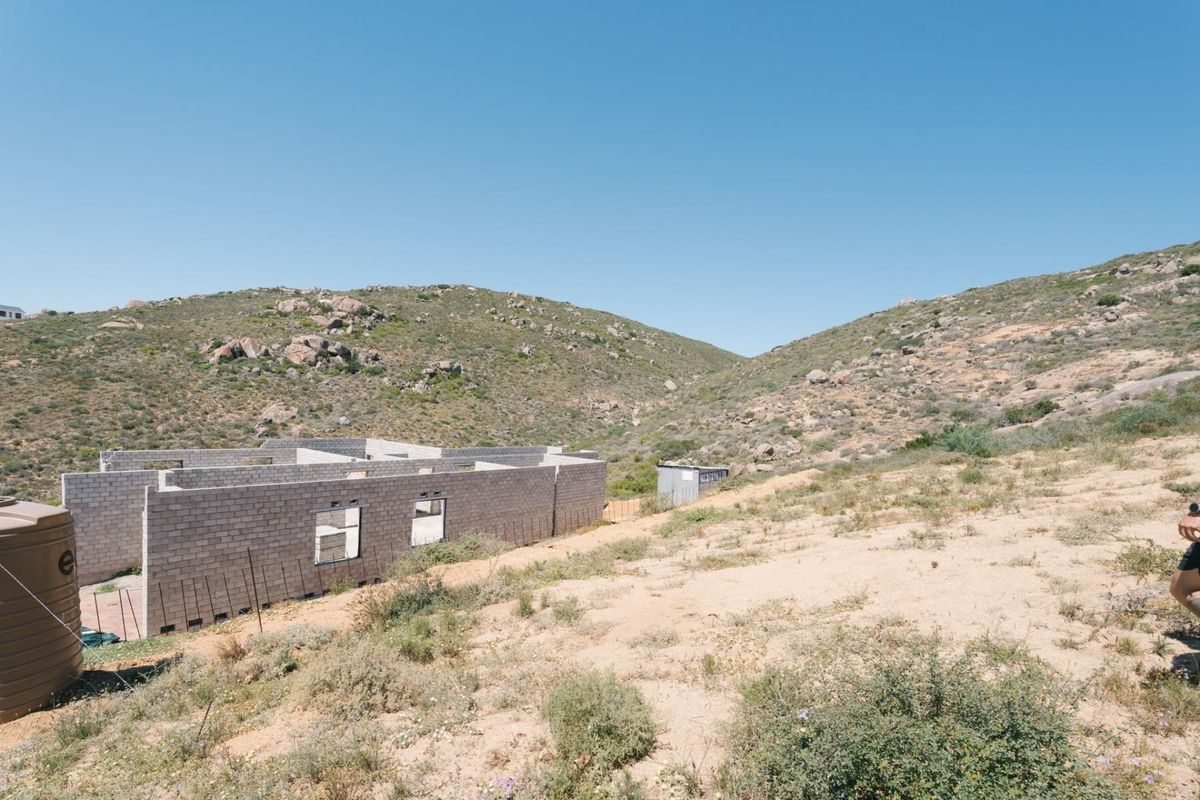 A view of a residential property under construction with concrete block walls and a water storage tank set against a hilly landscape.