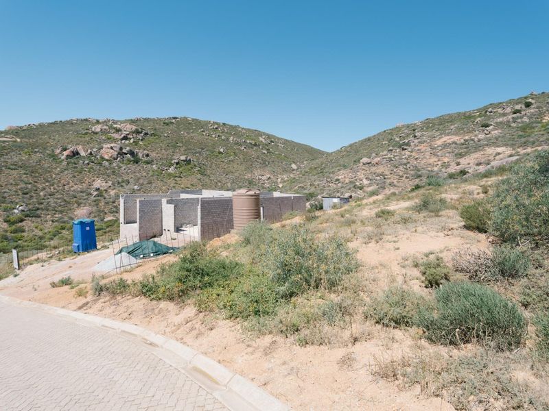 A vacant residential plot featuring an incomplete concrete block structure and a water storage tank, set against a natural hilly landscape.