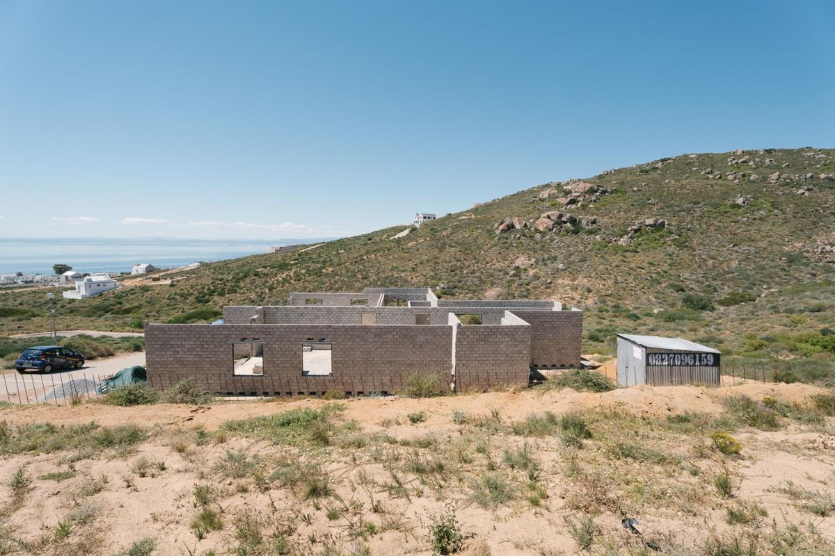 An aerial view of a residential property under construction, featuring concrete block walls and a metal storage shed on a hillside plot.