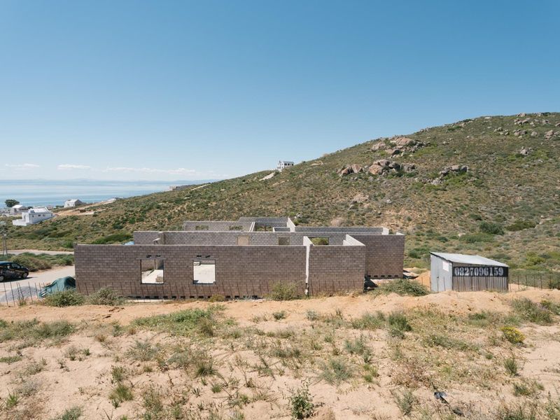 An aerial view of a residential property under construction, featuring concrete block walls and a metal storage shed on a hillside plot.