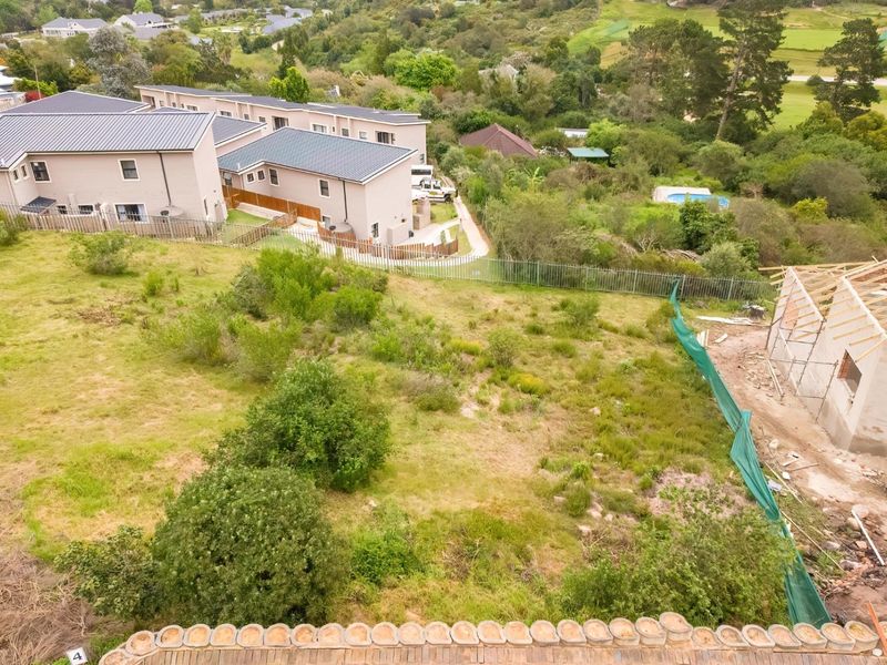 Aerial view of a vacant residential plot currently under development, featuring surrounding greenery and established residential properties in the background.