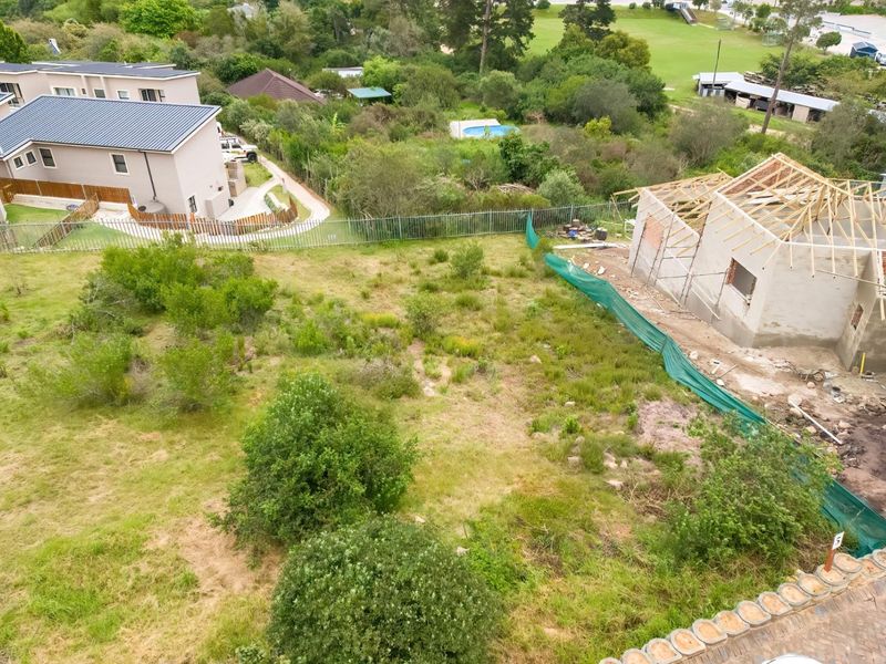 Aerial view of a residential vacant land plot featuring a partially constructed building with timber roof trusses and surrounding natural vegetation.