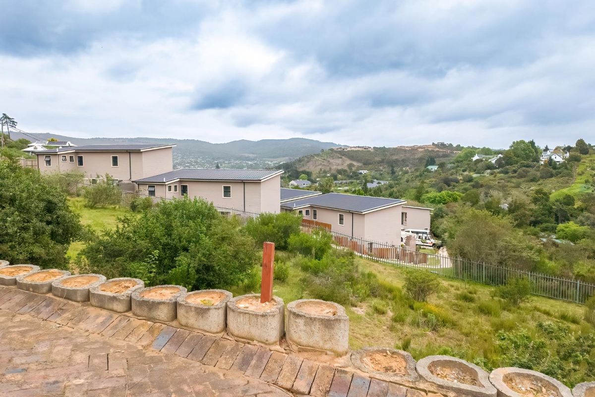 Elevated view overlooking a residential estate with surrounding hills and natural landscape, featuring a paved foreground and established perimeter fencing.