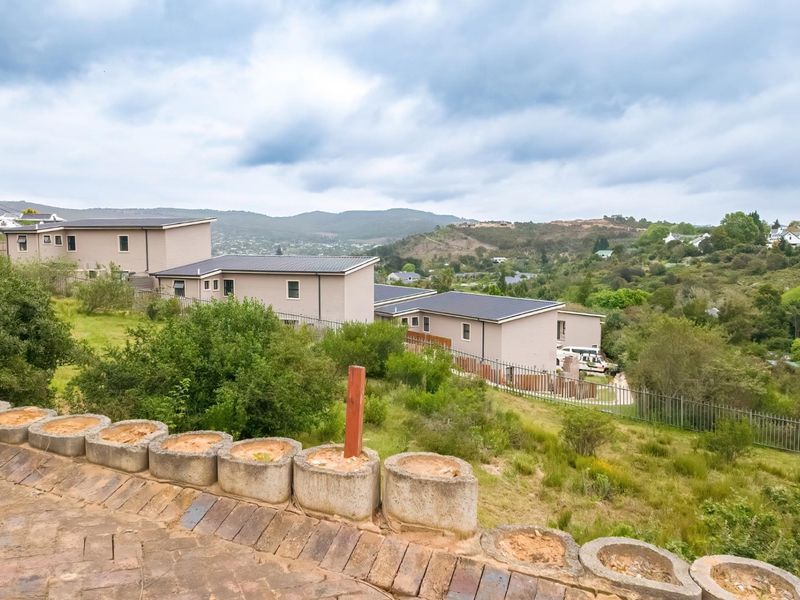Elevated view overlooking a residential estate with surrounding hills and natural landscape, featuring a paved foreground and established perimeter fencing.