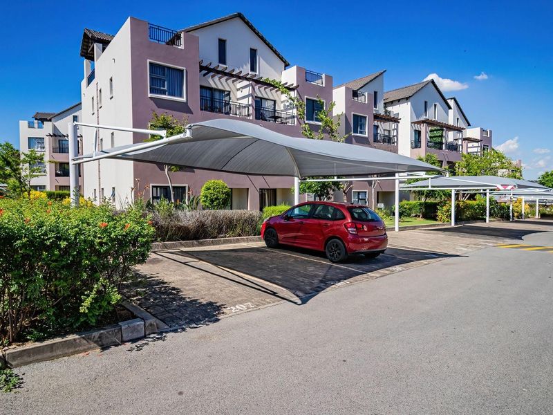 Exterior view of a modern apartment complex featuring covered parking bays and multi-story residential units with balconies.
