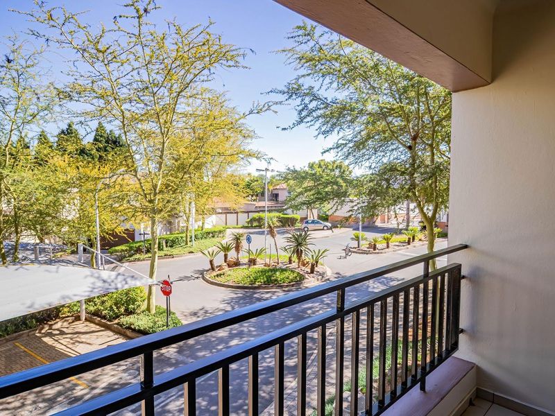 A clean, covered balcony featuring a metal balustrade and tiled flooring, offering an elevated view of the complex street and roundabout.
