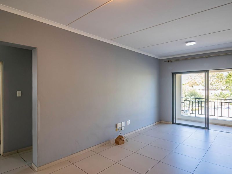 An empty, well-lit living area featuring neutral tiled floors, grey walls, and a sliding glass door leading to a private balcony.