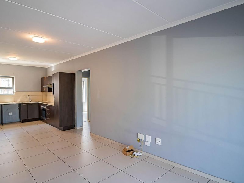 An open-plan living and kitchen area featuring modern dark cabinetry, built-in appliances, neutral tiled flooring, and a spacious layout.