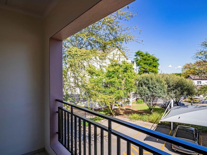 A private balcony featuring a metal balustrade and tiled flooring, offering an elevated view of the complex grounds and parking area.
