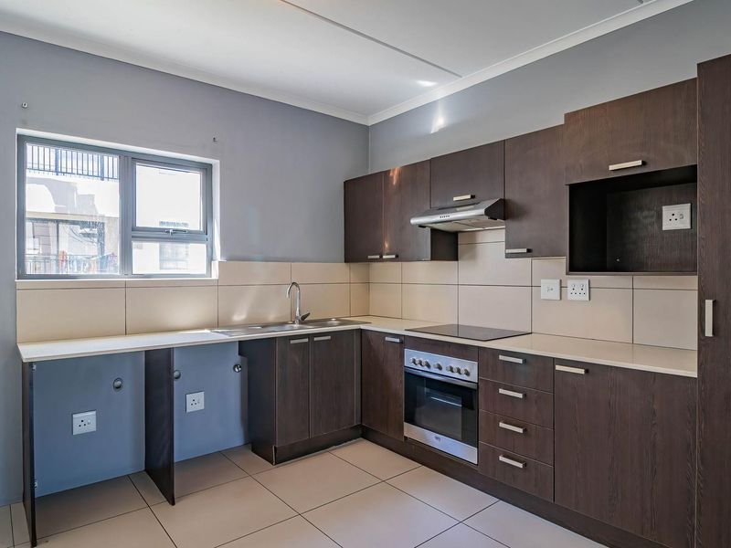 A clean, modern kitchen featuring dark wood cabinetry, integrated oven and hob, tiled splashback, and tiled flooring, offering a functional and well-maintained workspace.