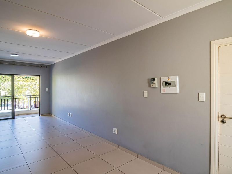 A spacious, empty living area featuring neutral grey walls, tiled flooring, and a sliding glass door leading to a balcony.