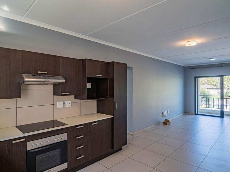 Spacious open-plan kitchen and living area featuring modern dark wood cabinetry, built-in appliances, tiled flooring, and direct access to a private balcony.