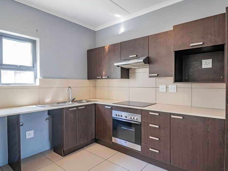 A clean, modern kitchen featuring dark wood cabinetry, integrated oven and hob, tiled splashbacks, and dedicated plumbing connections for appliances.