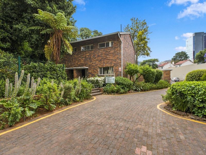 Front view of a two-story brick apartment building featuring a paved driveway and established garden landscaping.