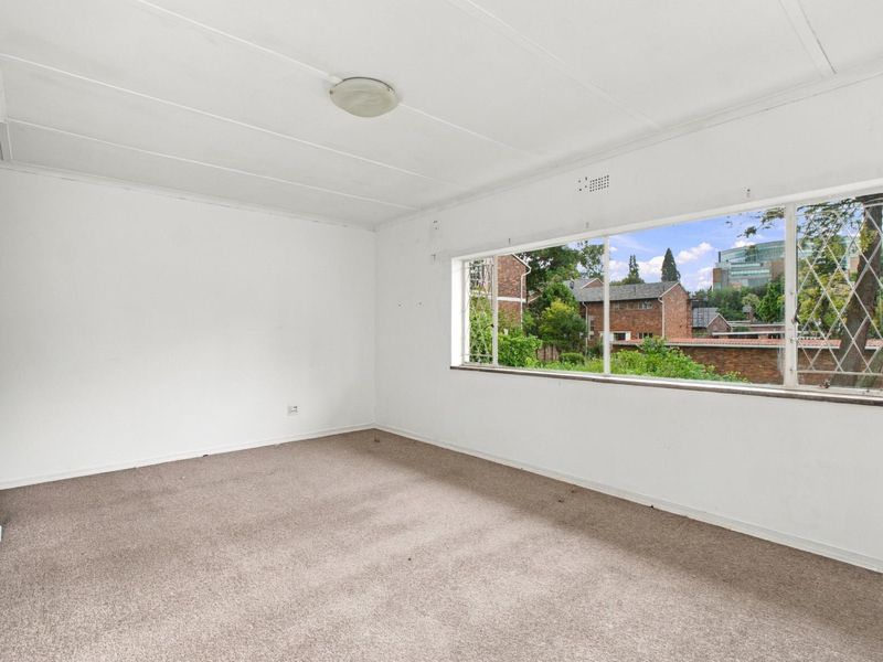 An empty bedroom featuring built-in cupboards, carpeted flooring, and a large window providing natural light and a view of the surrounding neighborhood.