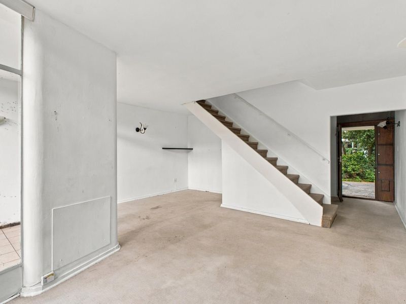An empty living room featuring a staircase, neutral wall finishes, and carpeted flooring, offering a blank canvas for renovation and interior design updates.