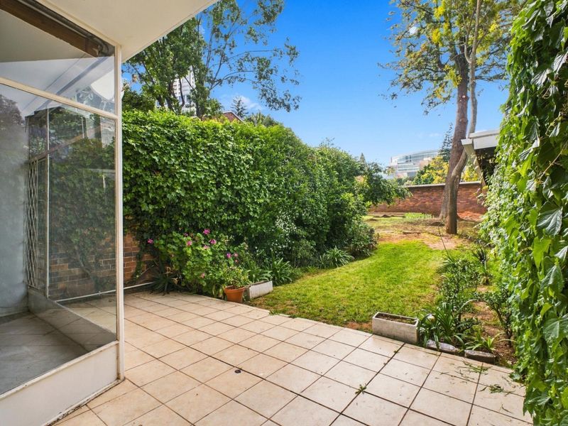 A private outdoor patio area featuring tiled flooring, adjacent to a garden space with established greenery and brick boundary walls.