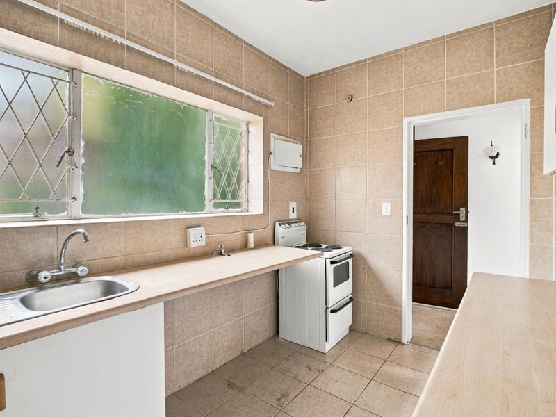 A functional kitchen featuring tiled walls and flooring, a stainless steel sink, laminate countertops, and a freestanding stove, offering potential for modernization.