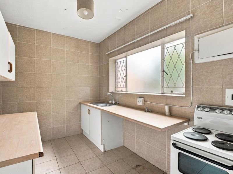 A functional kitchen featuring tiled walls and flooring, built-in cabinetry with laminate countertops, and an electric stove, offering potential for modernization.