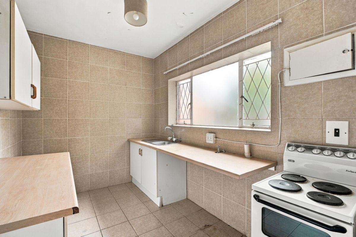 A functional kitchen featuring tiled walls and flooring, built-in cabinetry with laminate countertops, and an electric stove, offering potential for modernization.