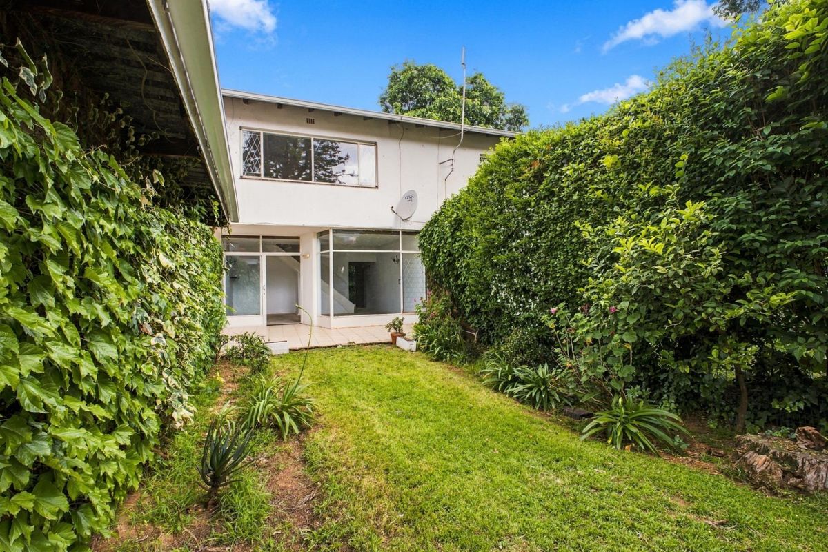 Rear view of the apartment featuring a small tiled patio, a private lawn area, and established garden hedges.
