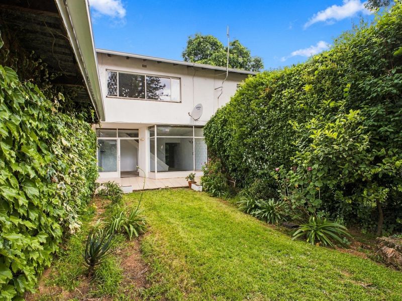 Rear view of the apartment featuring a small tiled patio, a private lawn area, and established garden hedges.