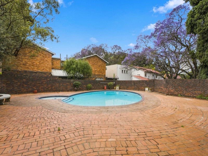 Communal outdoor pool area featuring a circular swimming pool surrounded by brick paving and a brick boundary wall.