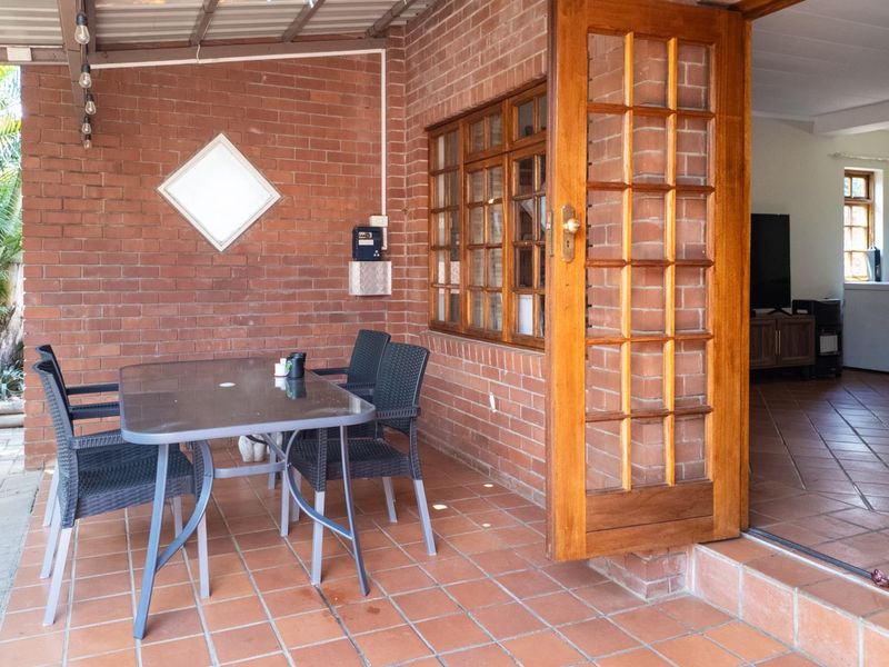 A covered patio area featuring exposed brick walls, terracotta tiling, and a timber-framed glass door providing access to the interior living space.