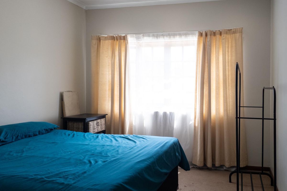 A bedroom featuring carpeted flooring and a window with installed curtain rails, providing natural light to the space.