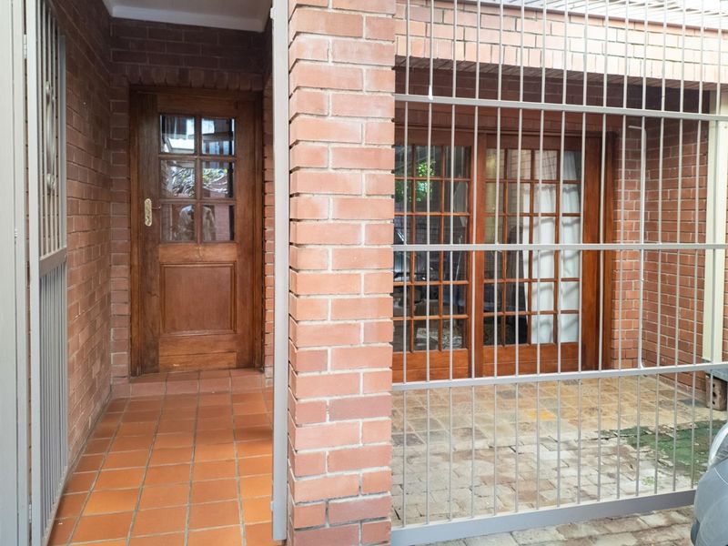 Front entrance area featuring exposed brickwork, tiled flooring, and secure metal gates leading to a timber-framed front door and sliding glass doors.