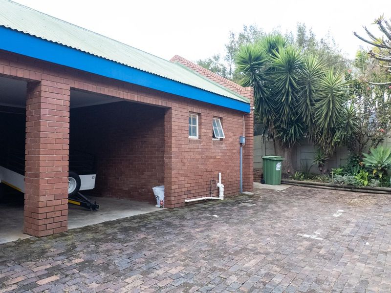 A brick-built garage with a corrugated metal roof and paved driveway area, featuring external plumbing and casement windows.