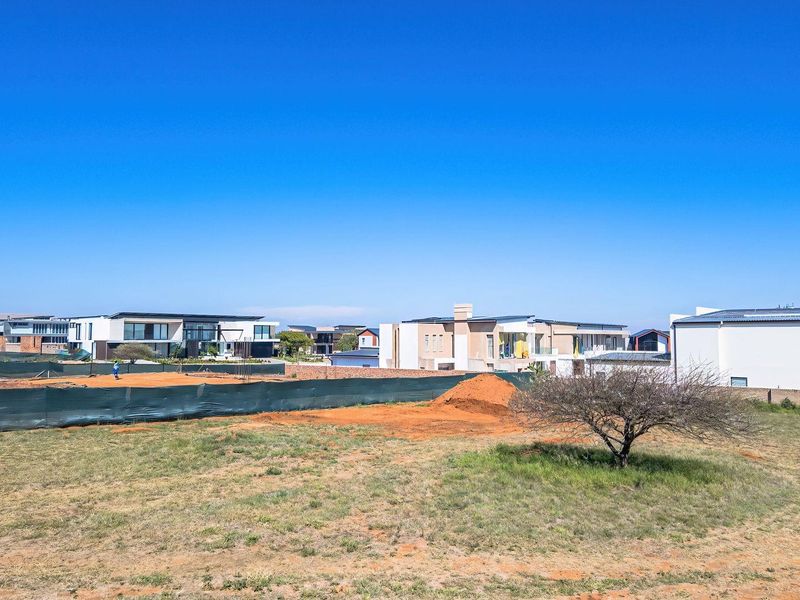 An aerial view of a vacant residential plot featuring natural ground cover and perimeter fencing, situated within a developed residential estate.