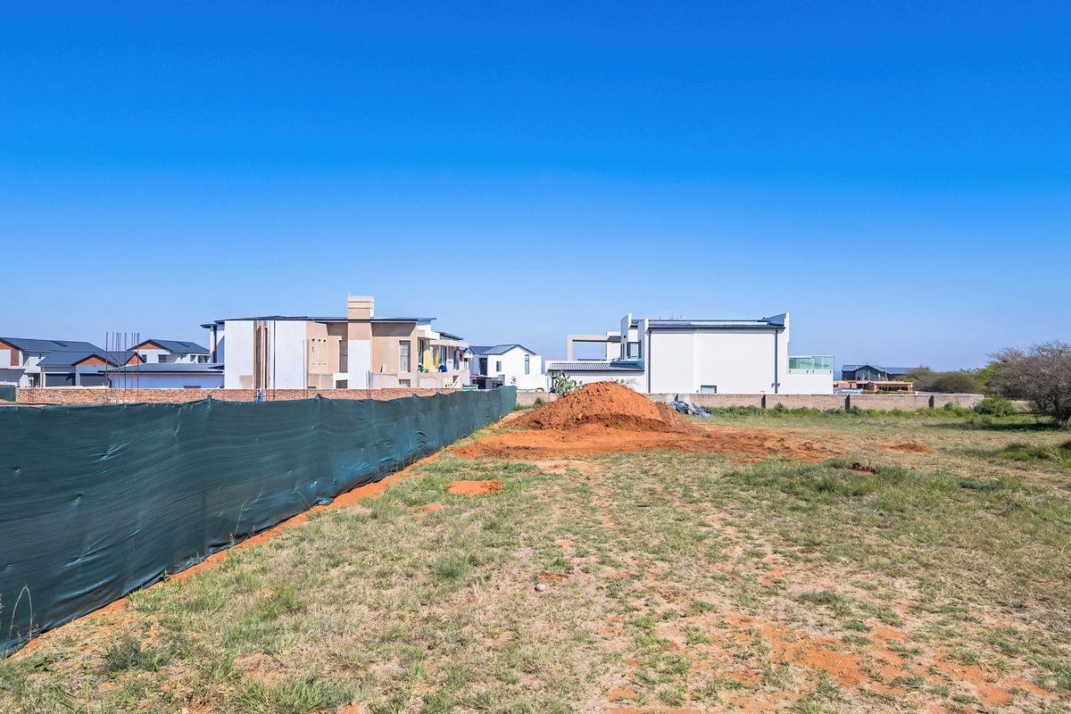 A vacant residential plot featuring a perimeter wall and temporary construction fencing, ready for development in a suburban neighborhood.