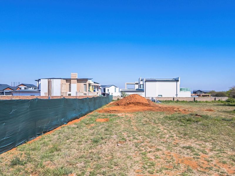 A vacant residential plot featuring a perimeter wall and temporary construction fencing, ready for development in a suburban neighborhood.